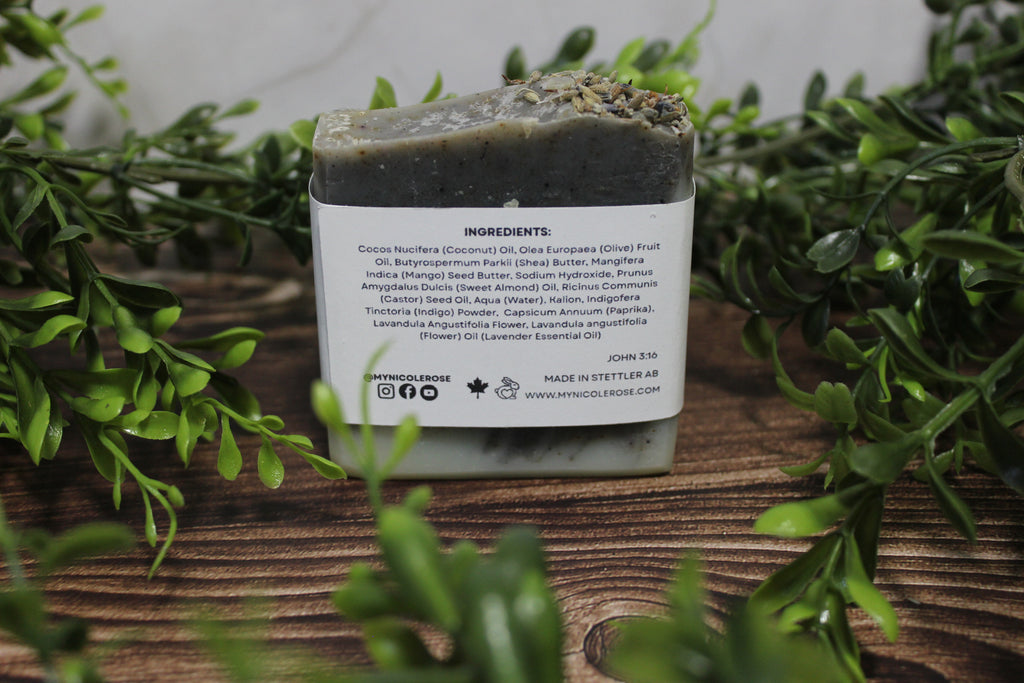 Bar of soap with a label on a wooden surface surrounded by greenery