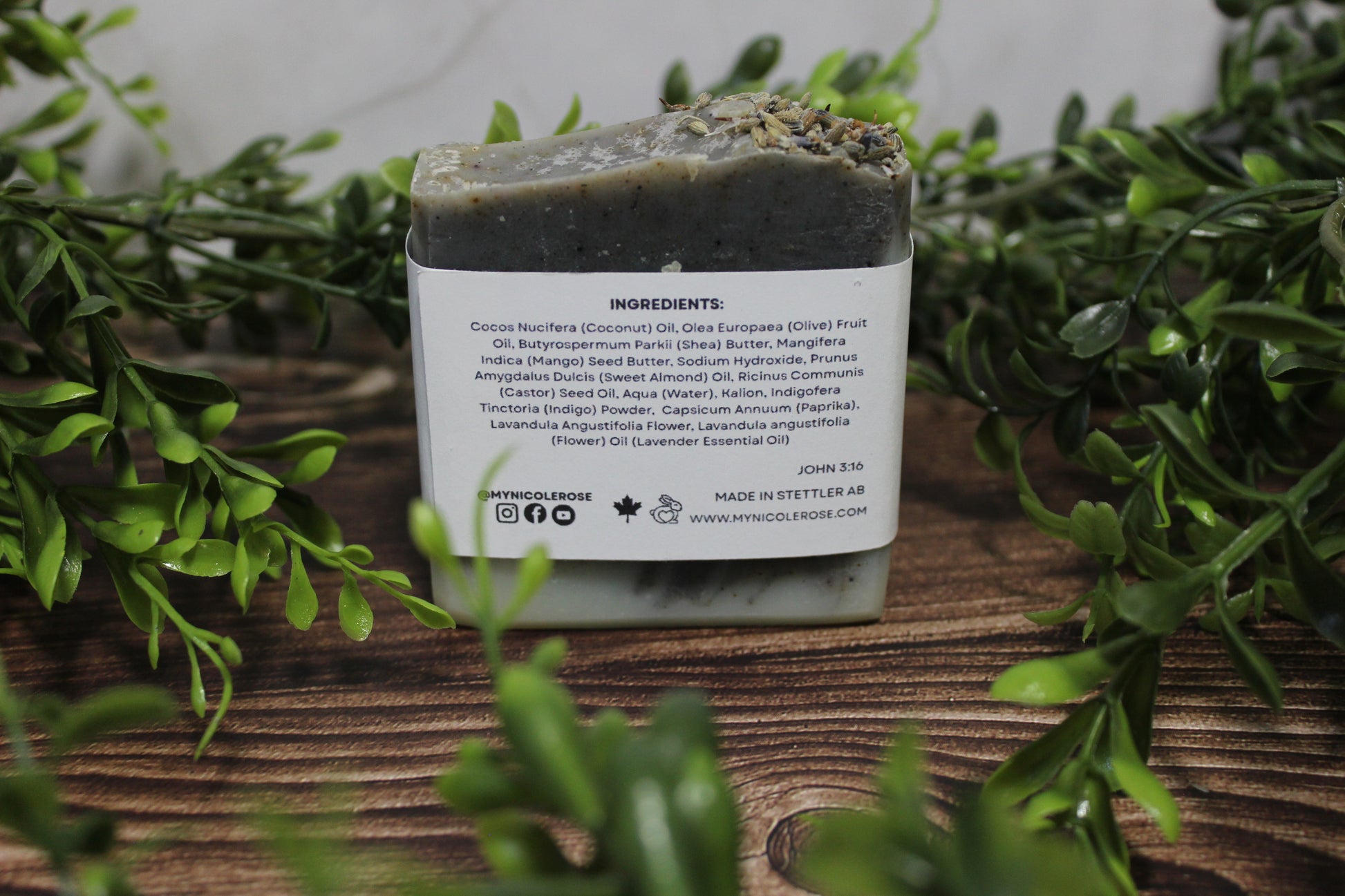 Bar of soap with a label on a wooden surface surrounded by greenery