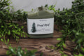 Green soap bar with a label on a wooden surface surrounded by greenery