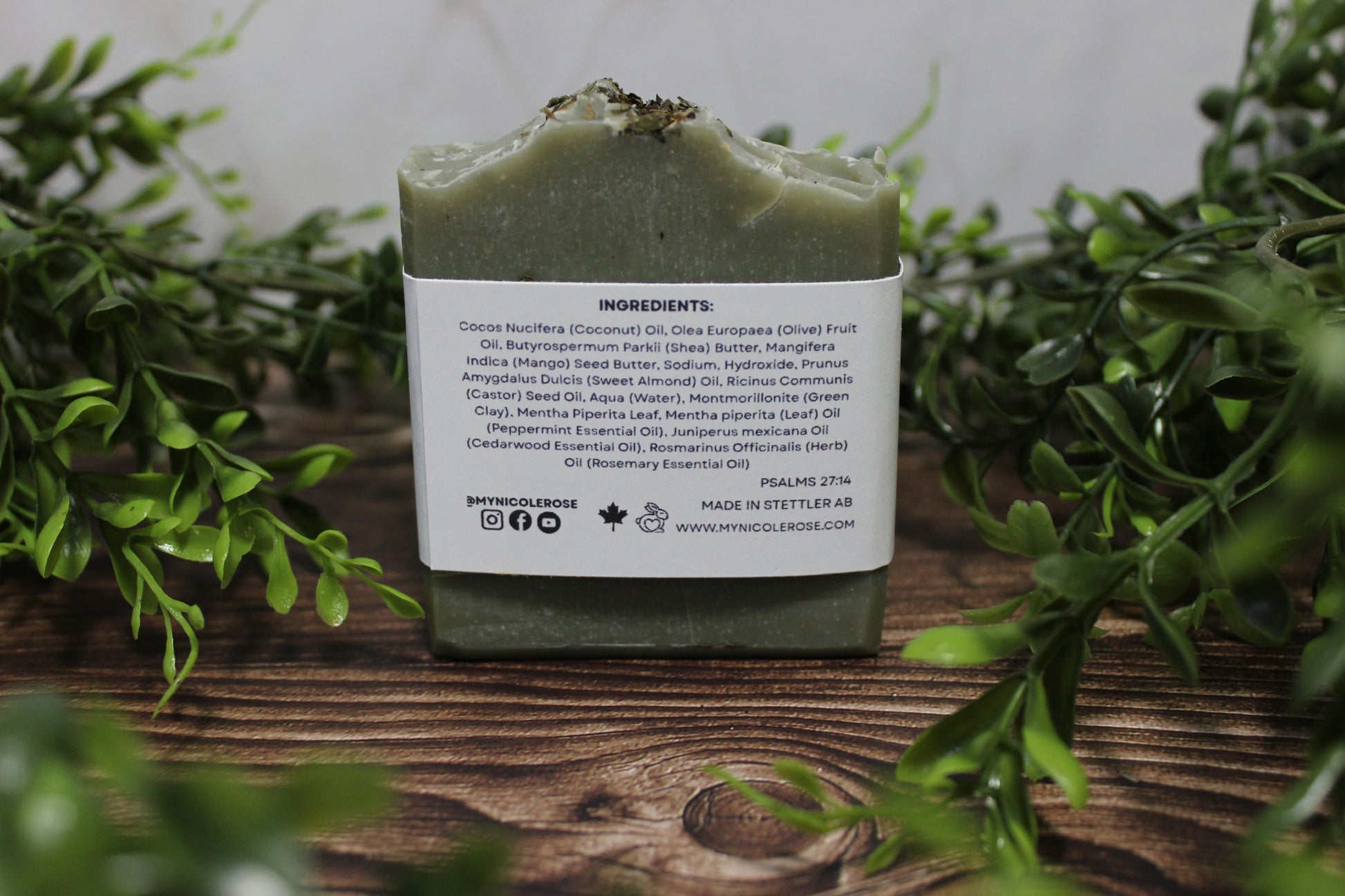 Green soap bar with a label on a wooden surface surrounded by greenery