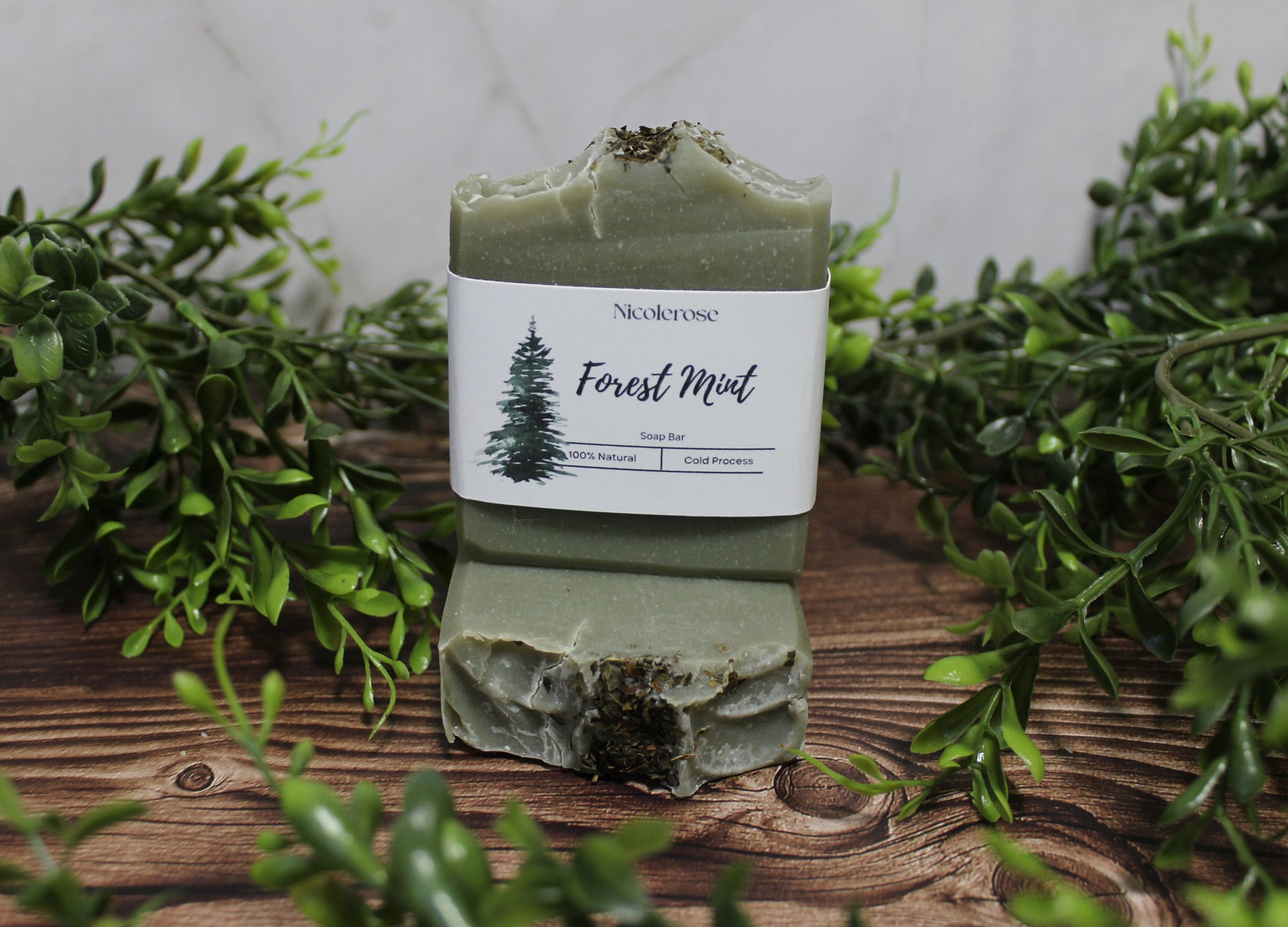 Green soap bar with 'Nicolerose' label on a wooden surface surrounded by greenery