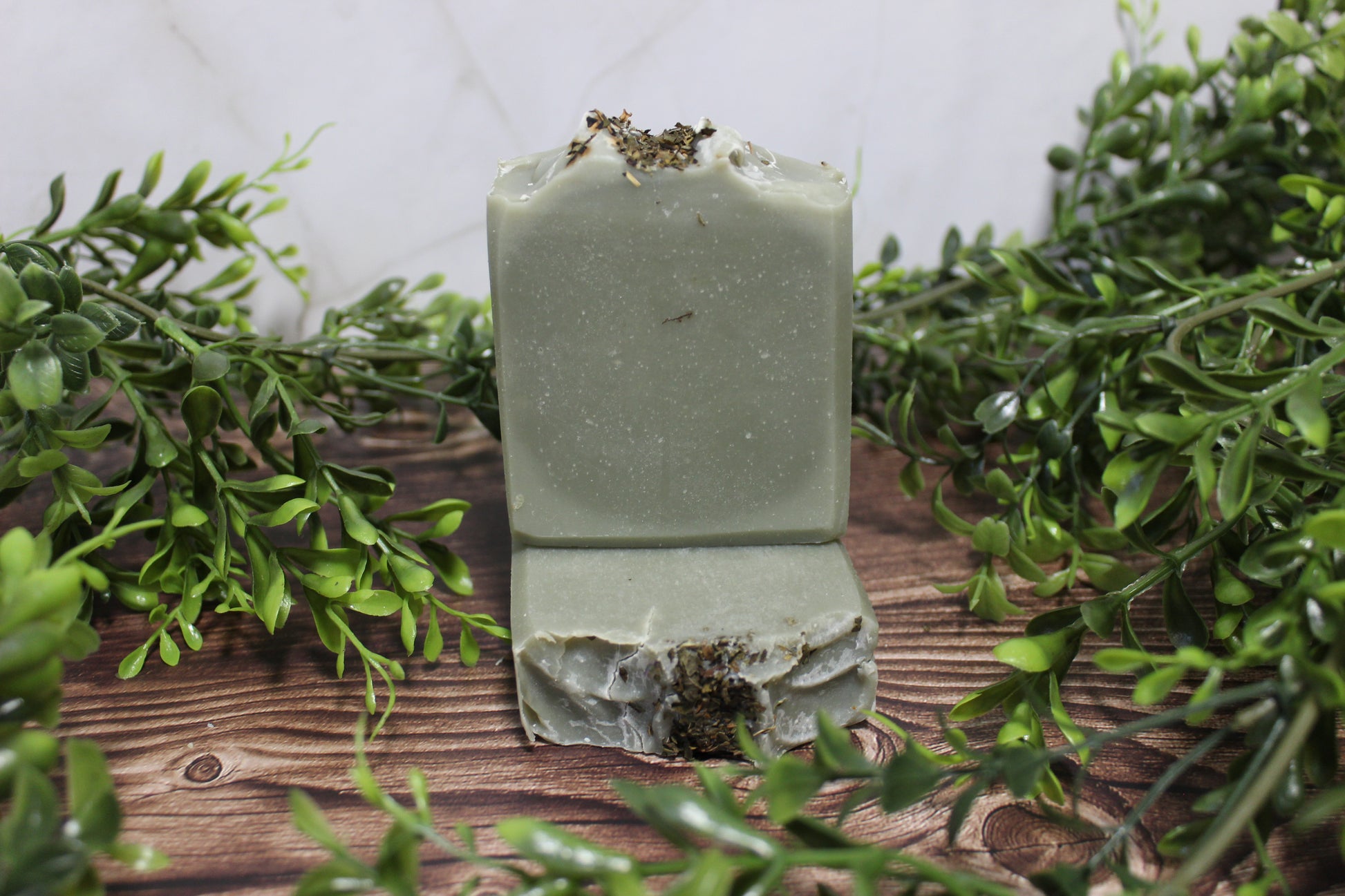 Green soap bar on a wooden surface with greenery around