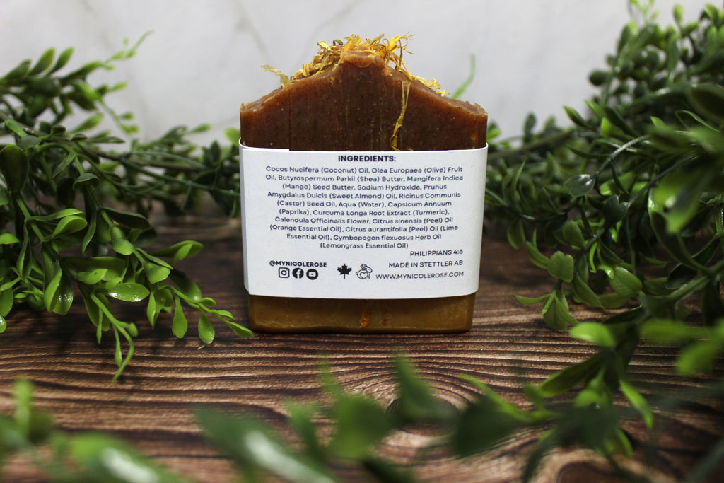 Bar of soap with a label on a wooden surface surrounded by greenery