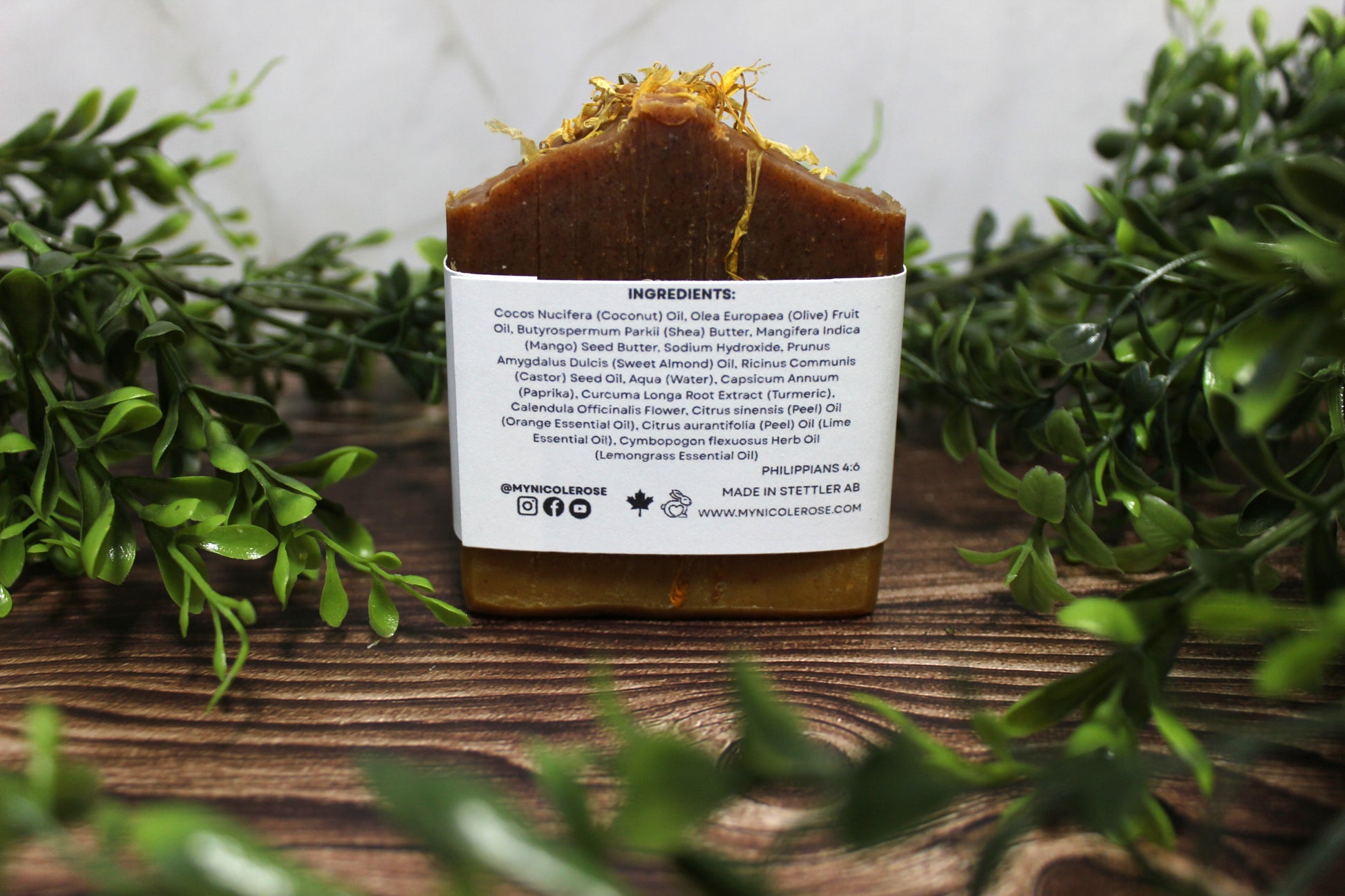 Bar of soap with a label on a wooden surface surrounded by greenery