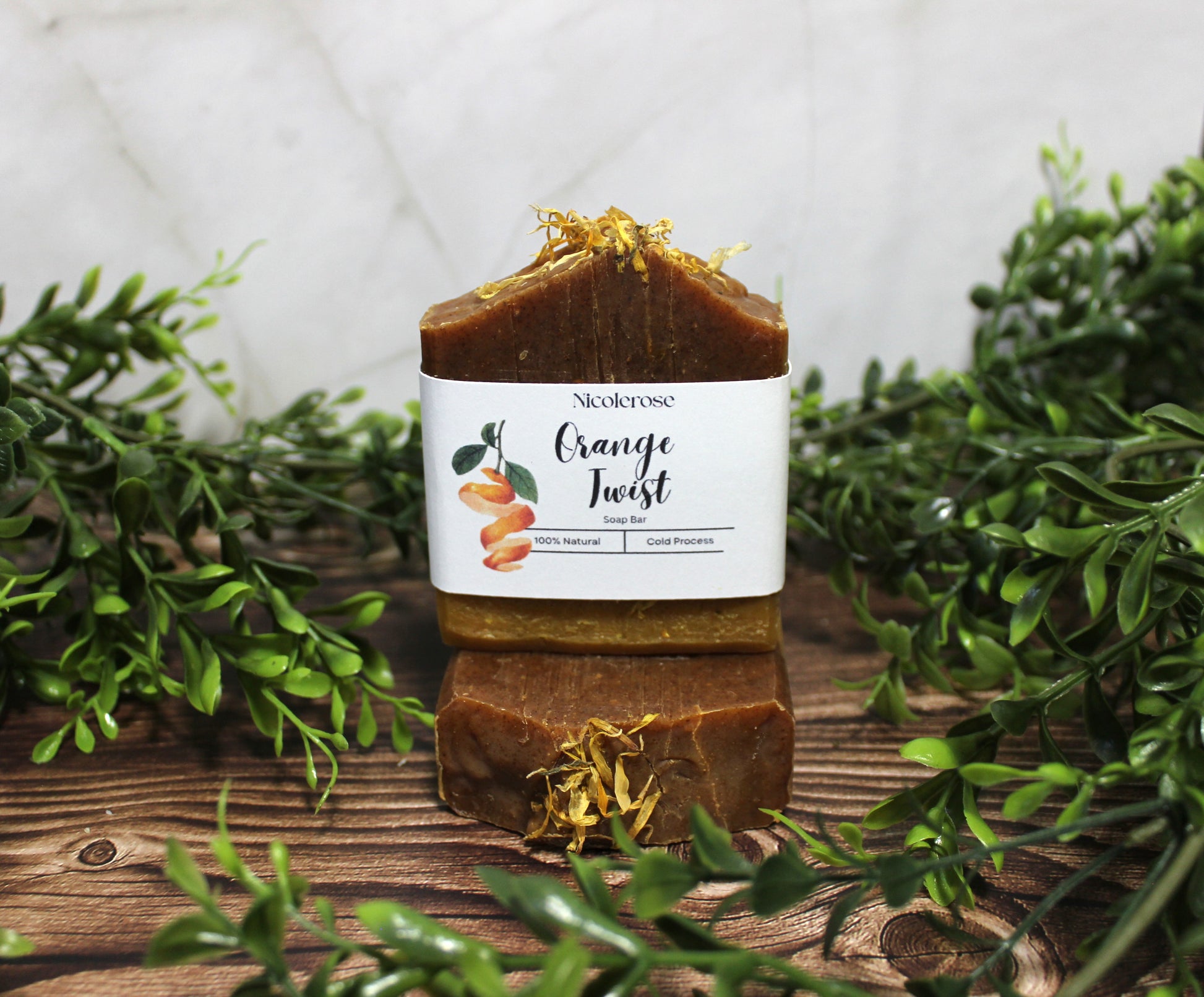 Bar of soap with 'Orange Twist' label on a wooden surface with greenery