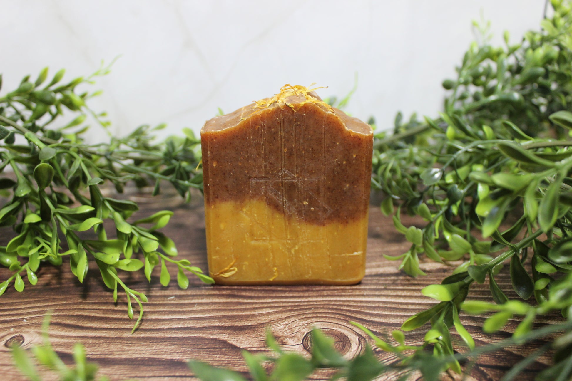 Square bar of soap with Orange and yellow gradient on a wooden surface with green foliage