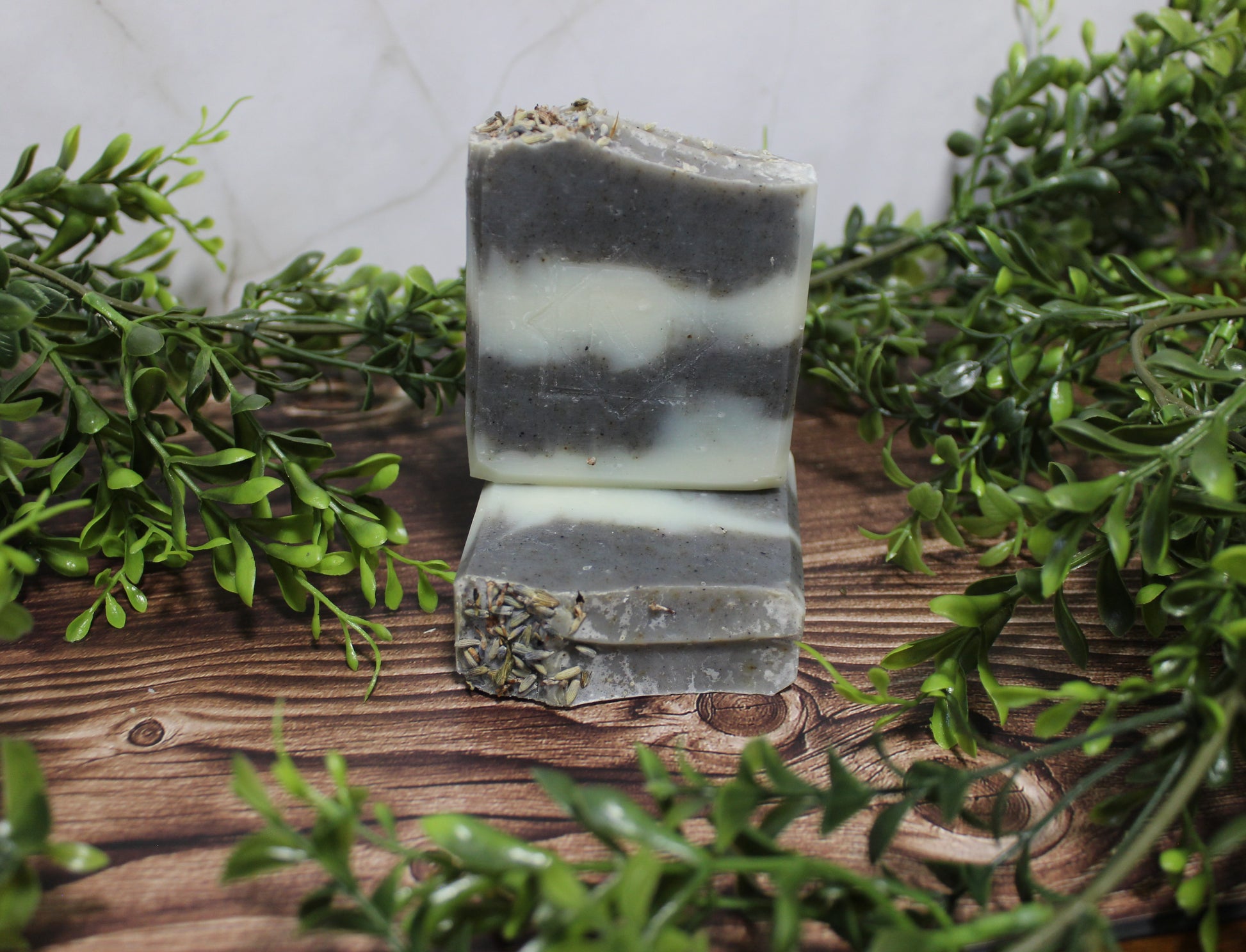 Stack of natural soap bars with greenery on a wooden surface