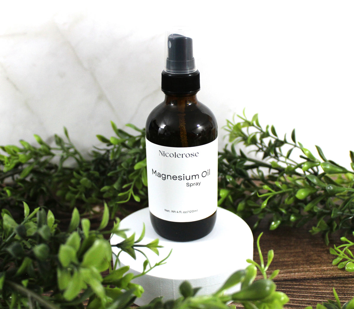 Bottle of Niceterose Magnesium Oil Spray surrounded by greenery on a white background