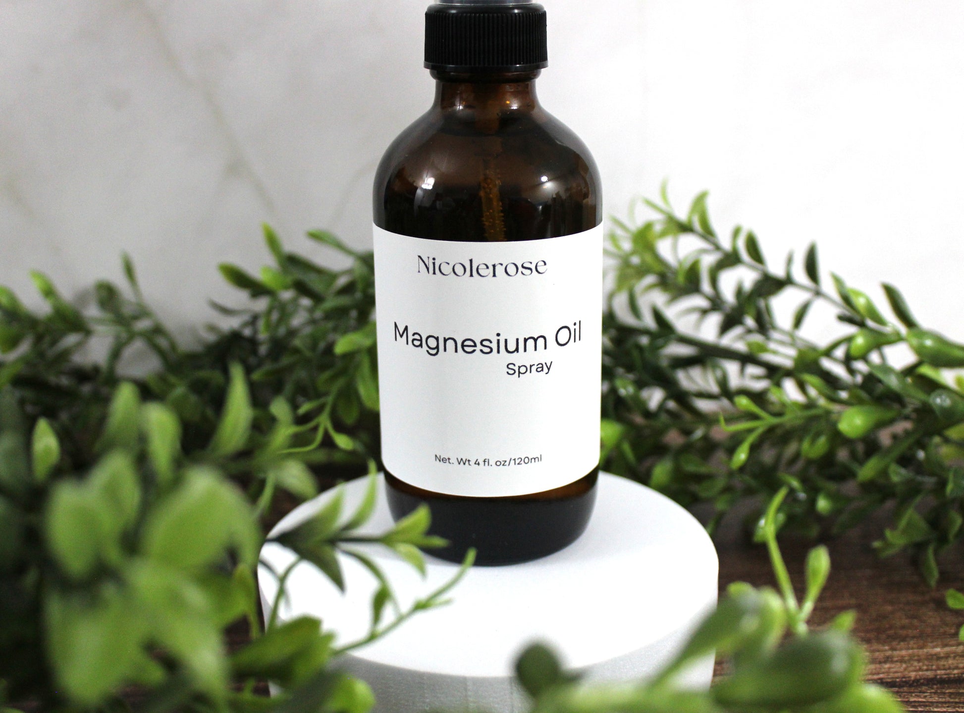 Bottle of Nicoleros magnesium oil spray surrounded by greenery on a white surface.