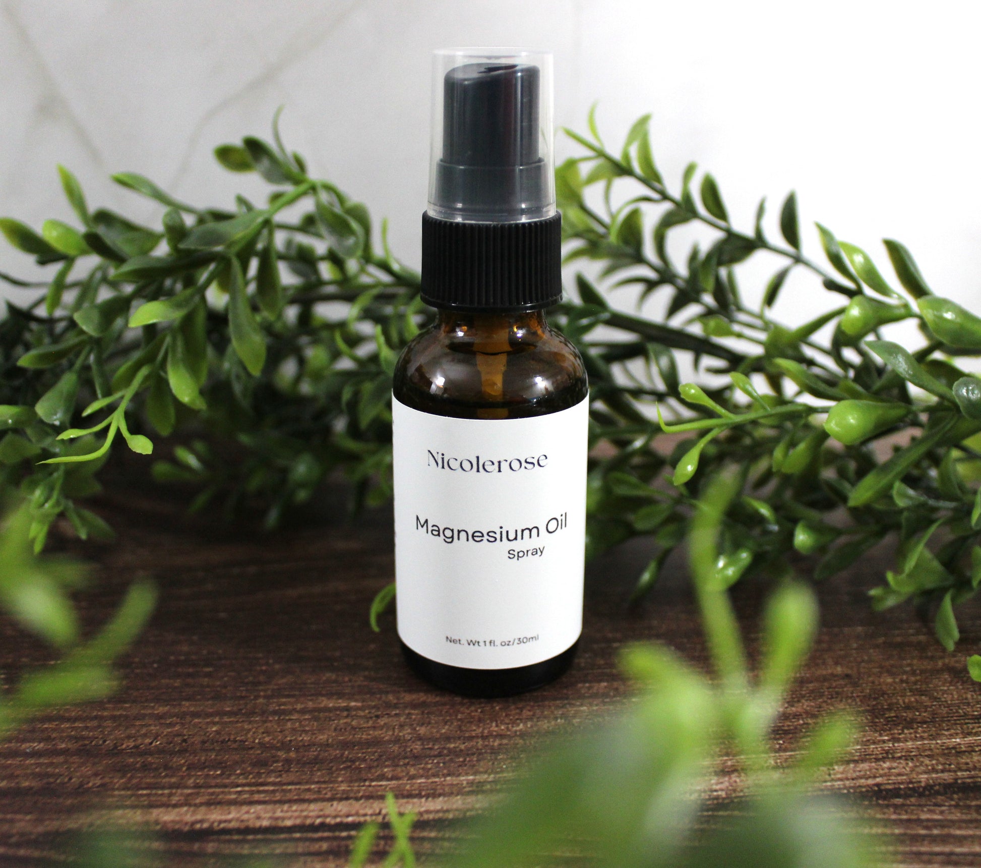 Bottle of Nicoleros Magnesium Oil Spray on a wooden surface with green leaves in the background