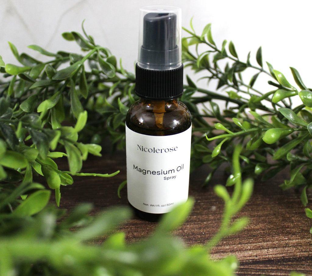 Bottle of Nicolerose Magnesium Oil Spray on a wooden surface with green leaves in the background