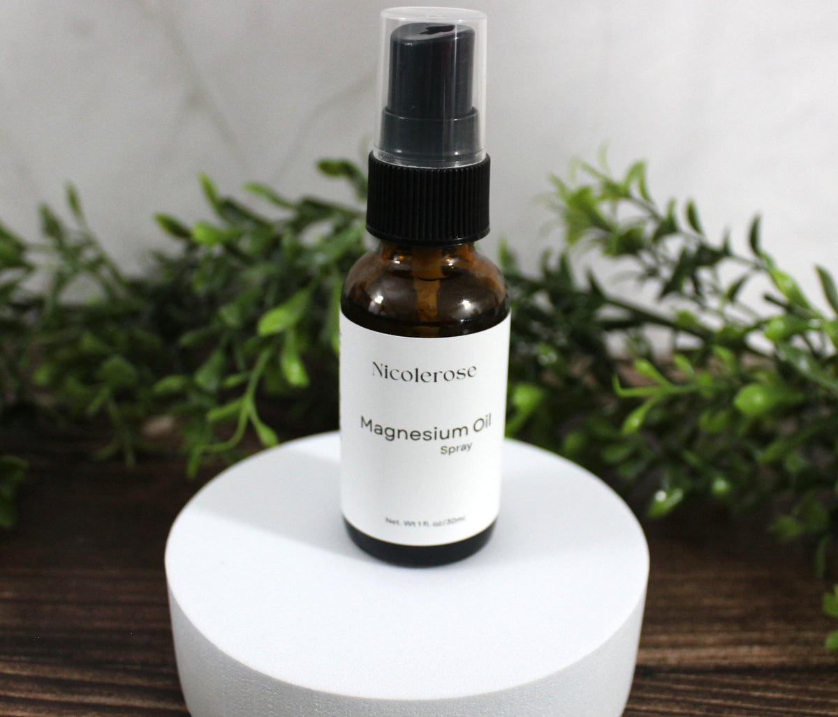Bottle of Nicoleros magnesium oil spray on a white pedestal with greenery in the background