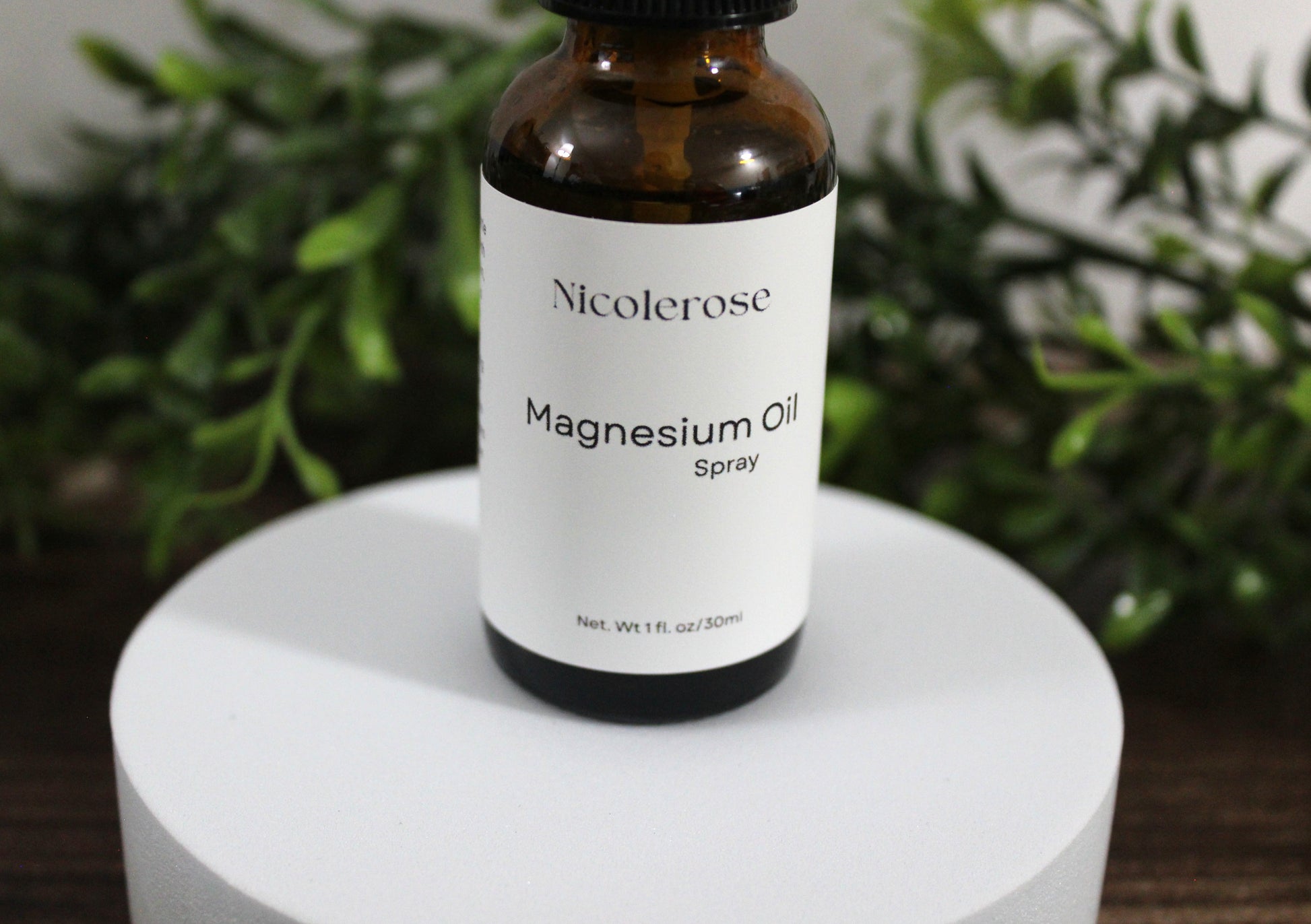Bottle of Nicoleros magnesium oil spray on a white surface with greenery in the background