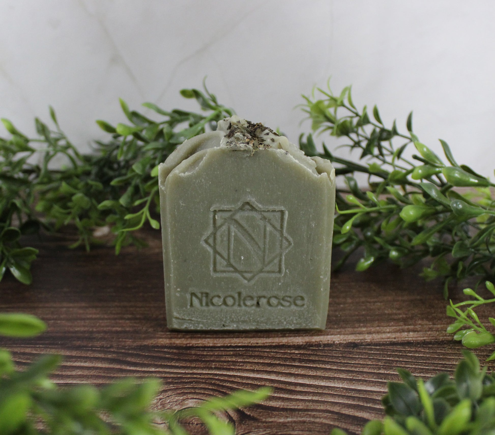 Green soap bar with 'NicoleRose' branding on a wooden surface with greenery.