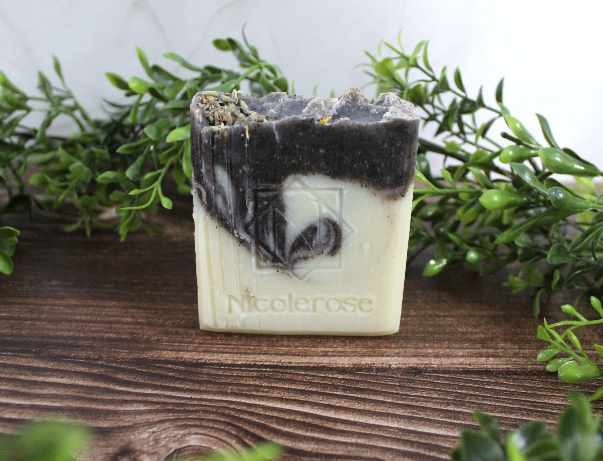 Bar of soap with 'Nicolerose' branding on a wooden surface with greenery in the background