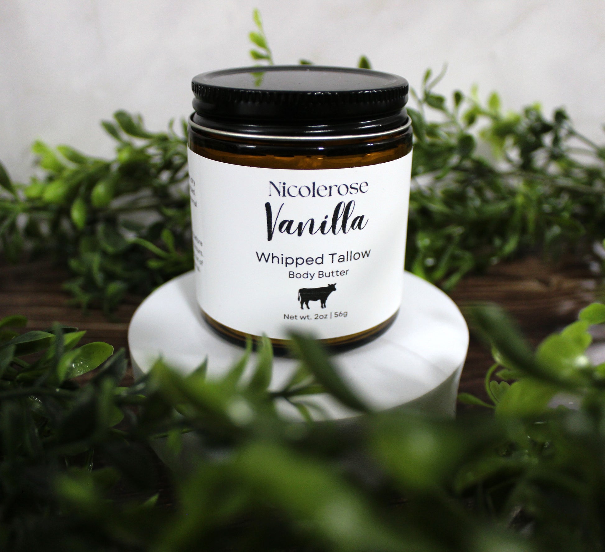 Jar of Nicolerose Vanilla Whipped Tallow Body Butter on a white stand with greenery in the background