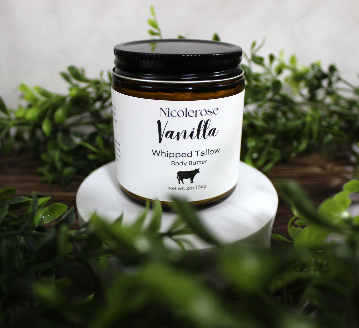 Jar of Nicolerose Vanilla Whipped Tallow Body Butter on a white stand with greenery in the background