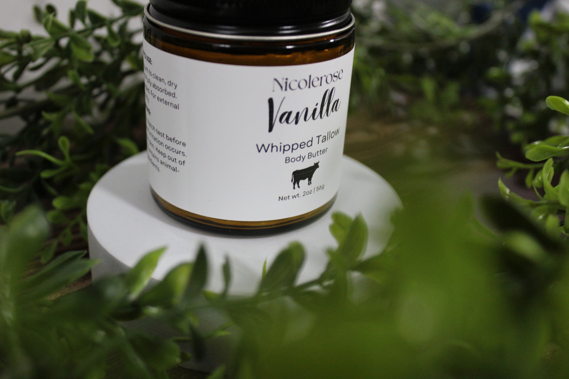 Jar of Nicoleros Vanilla Whipped Tailor Body Butter on a white stand with greenery in the background
