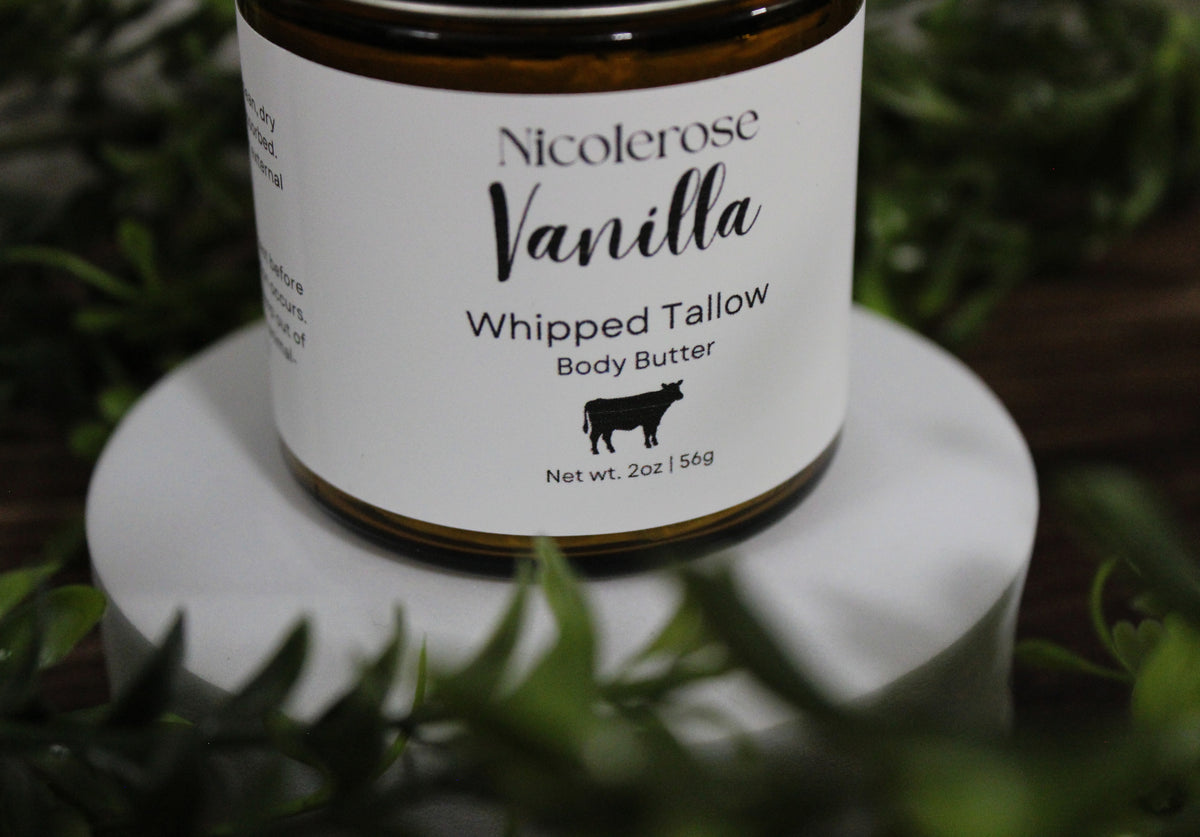 Jar of Nicoleros Vanilla Whipped Tallow Body Butter on a white stand with greenery in the background