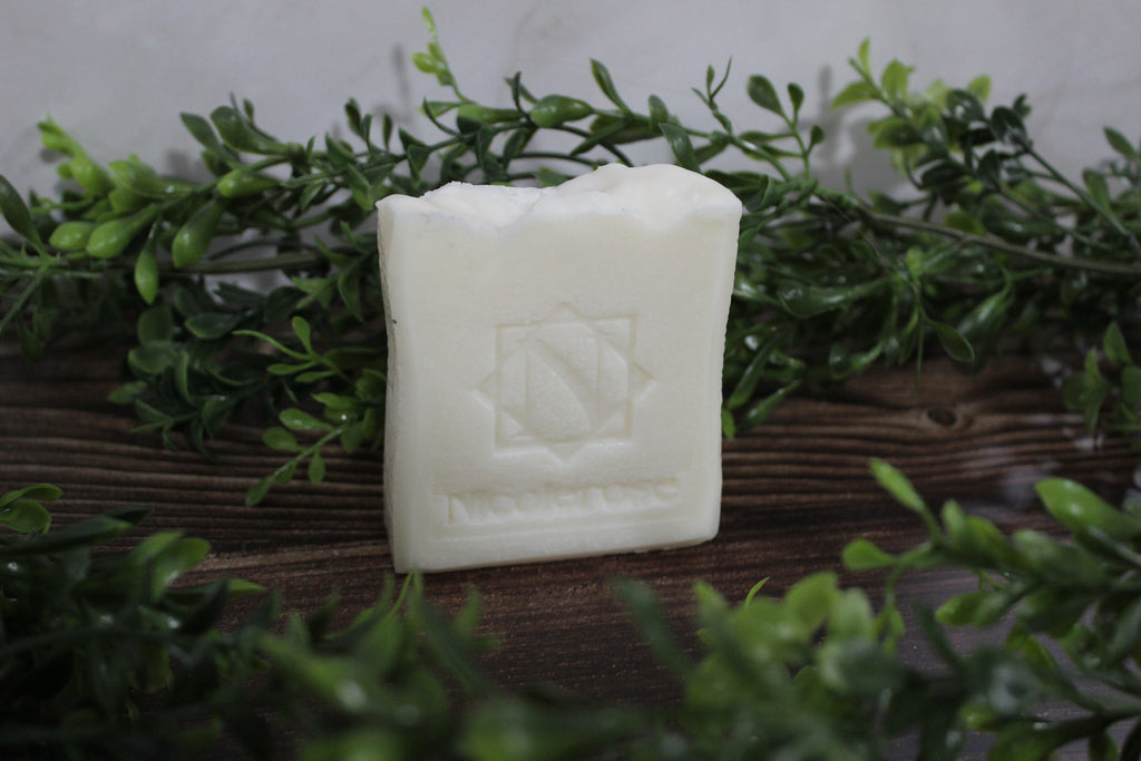 White soap bar with a logo on a wooden surface surrounded by green leaves