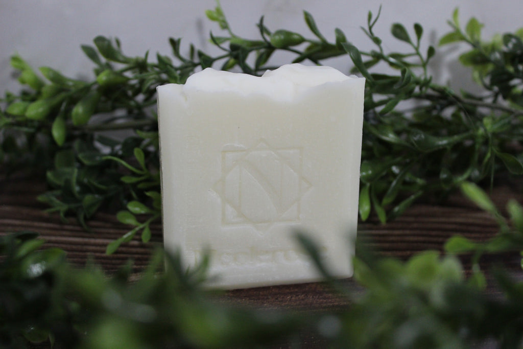 White bar of soap with a logo on a wooden block surrounded by green leaves