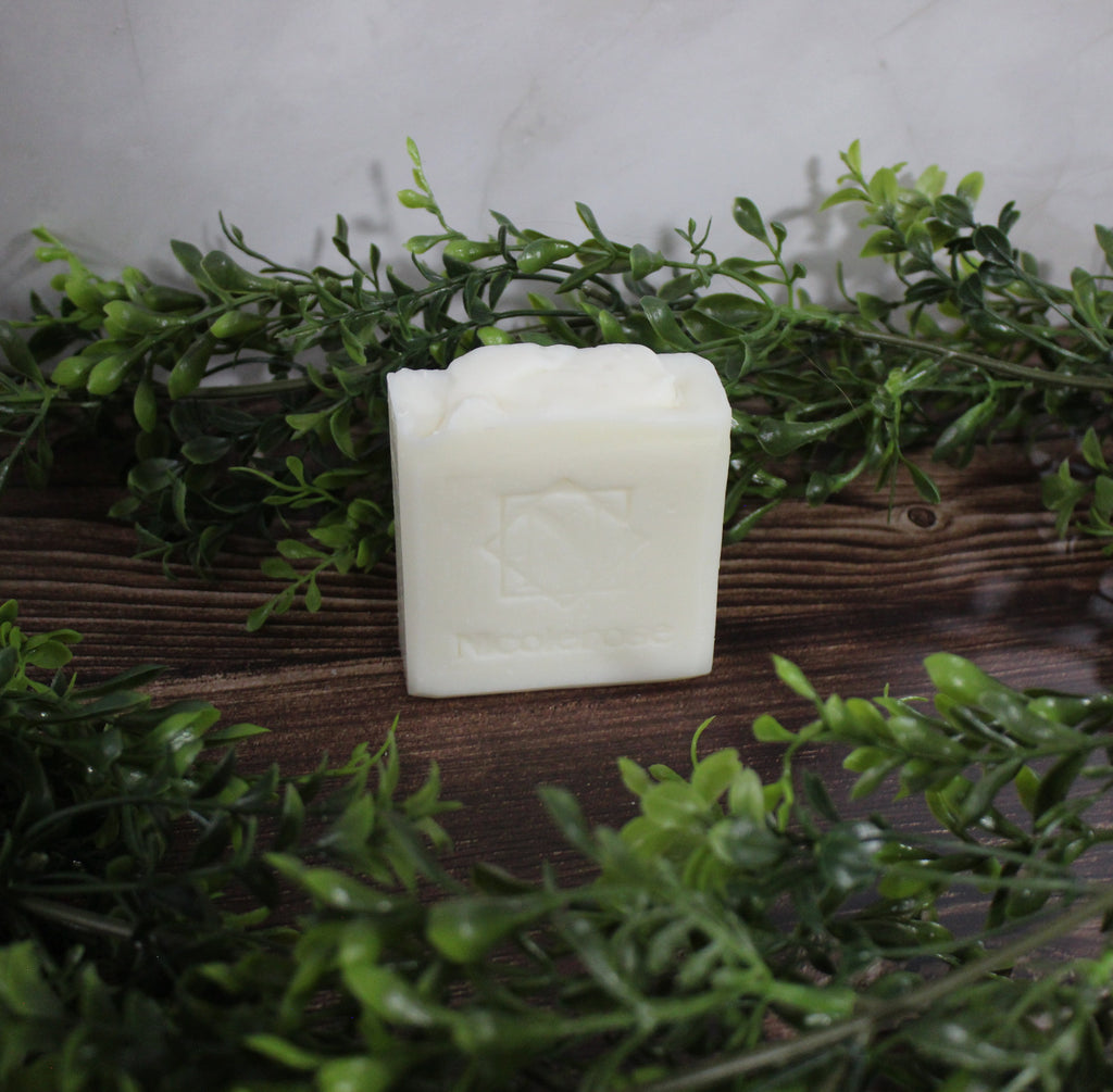 White bar of soap on a wooden surface with green leaves in the background