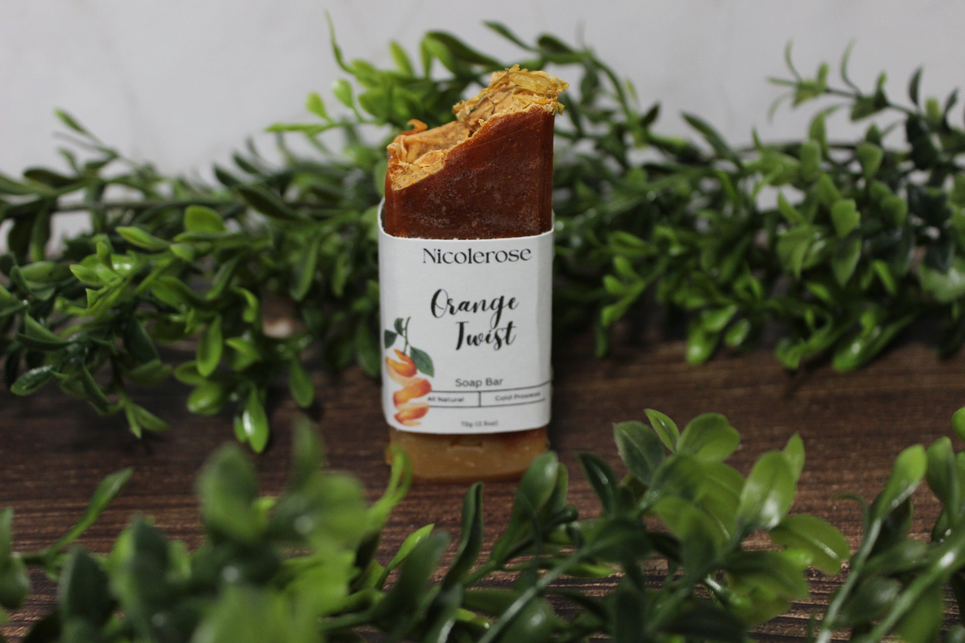 Nicolerose Orange Twist soap bar on a wooden surface with green foliage