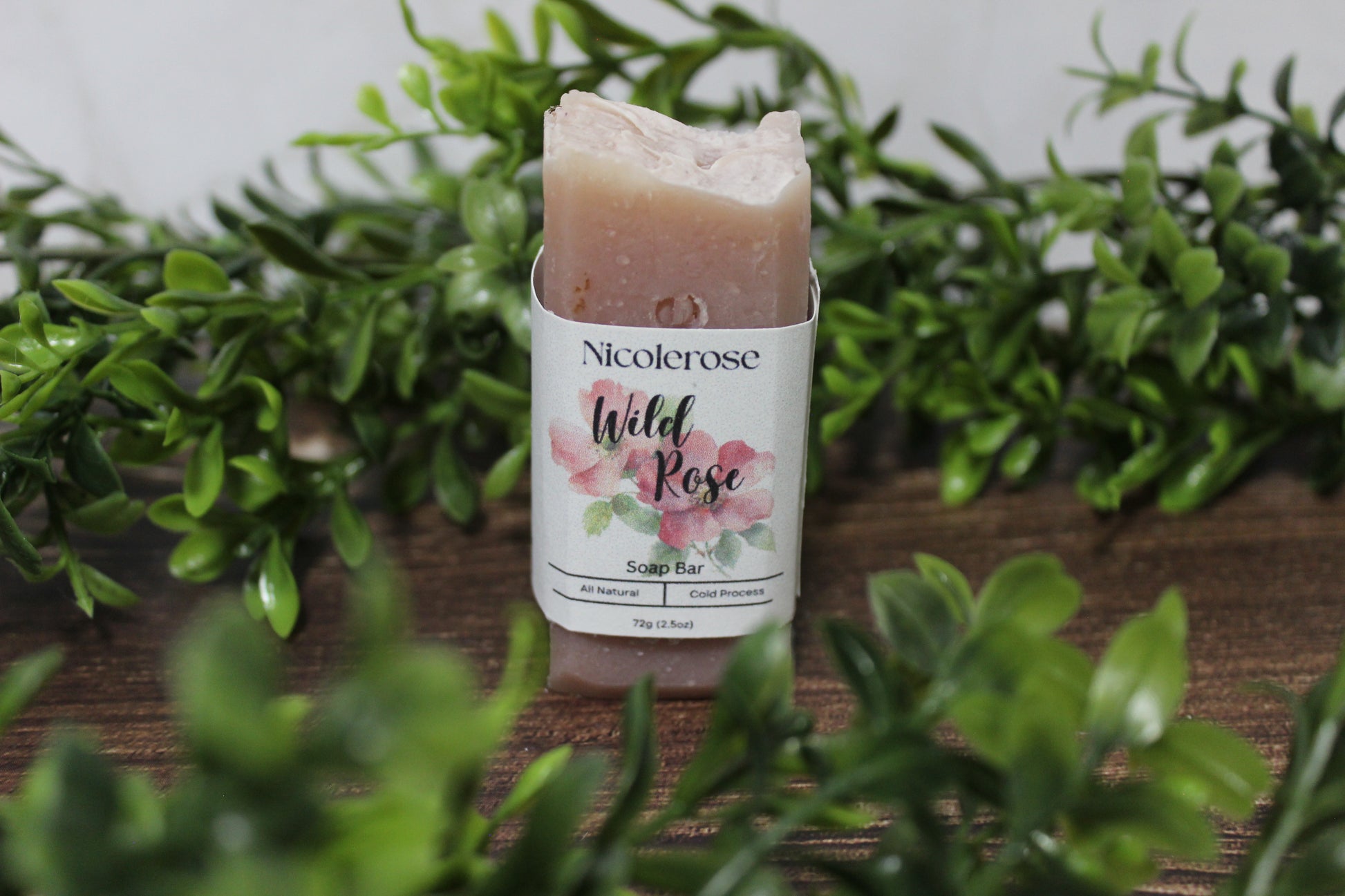 Nicolerose Wild Rose soap bar on a wooden surface with greenery in the background
