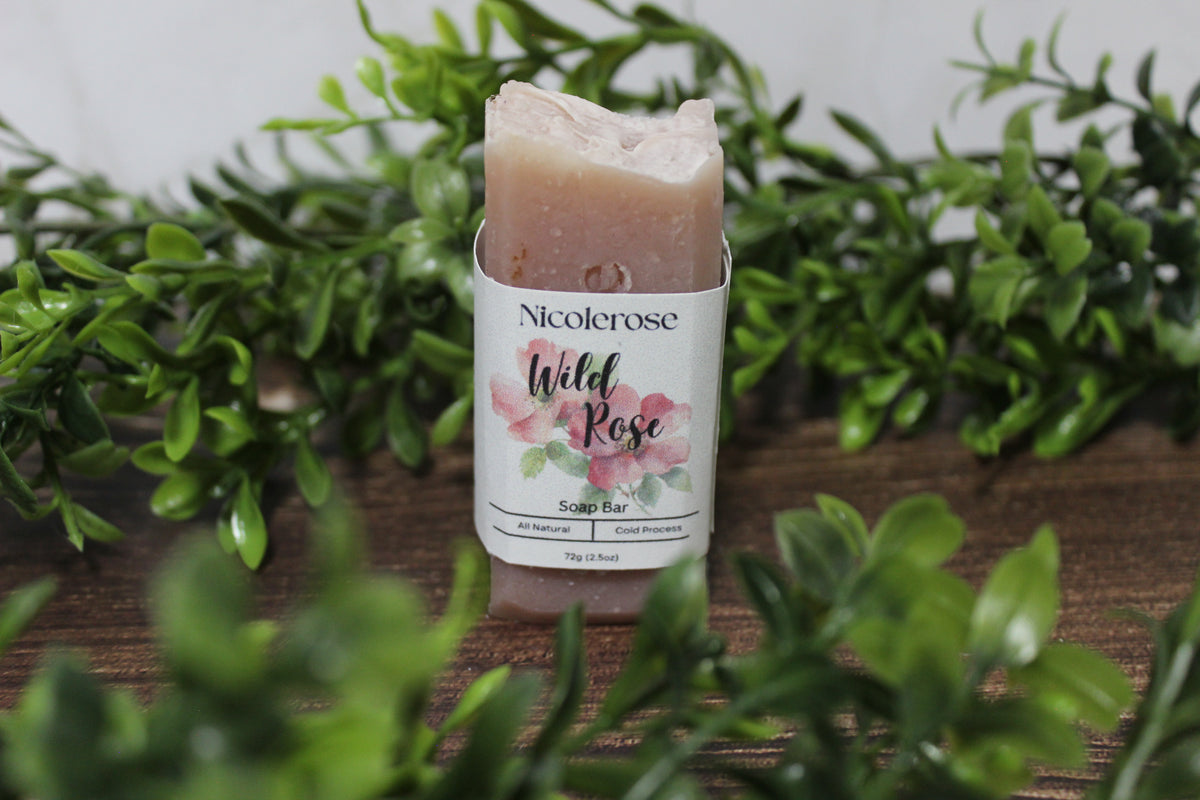Nicolerose Wild Rose soap bar on a wooden surface with greenery in the background