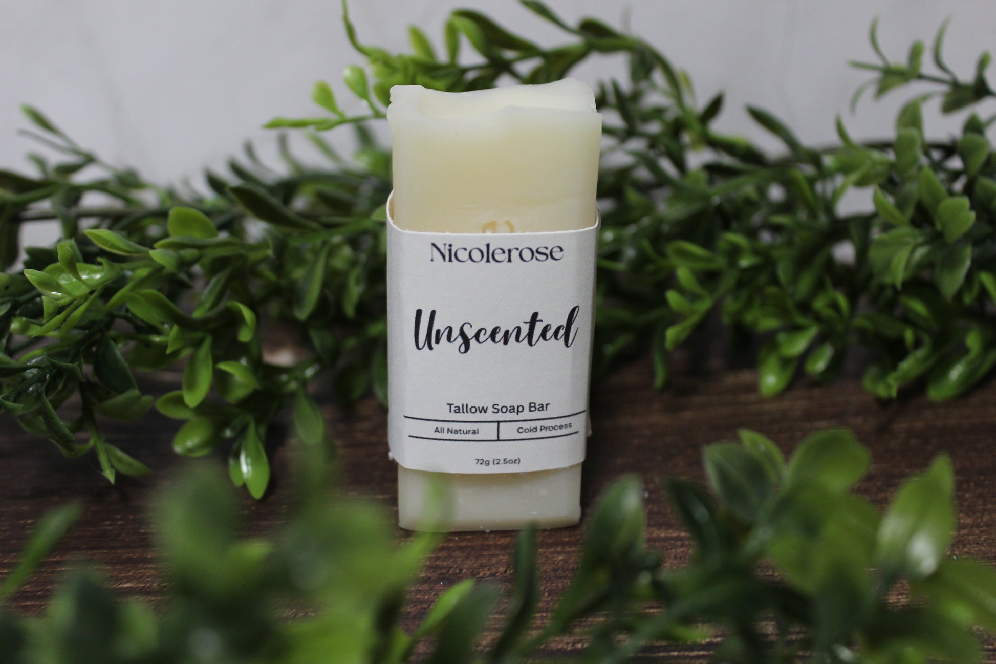 Nicolerose unscented tallow soap bar on a wooden surface with greenery in the background
