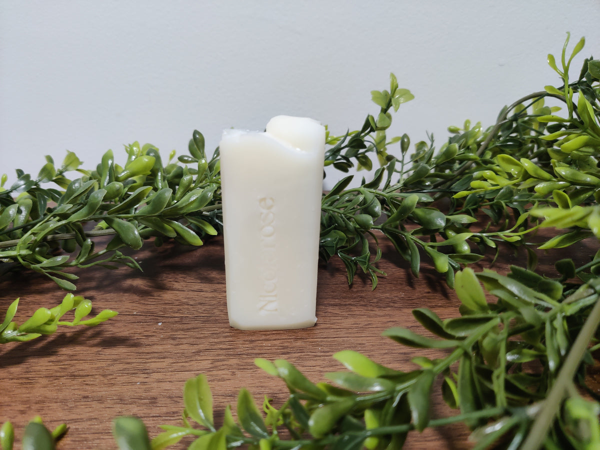 White candle on a wooden surface with green foliage