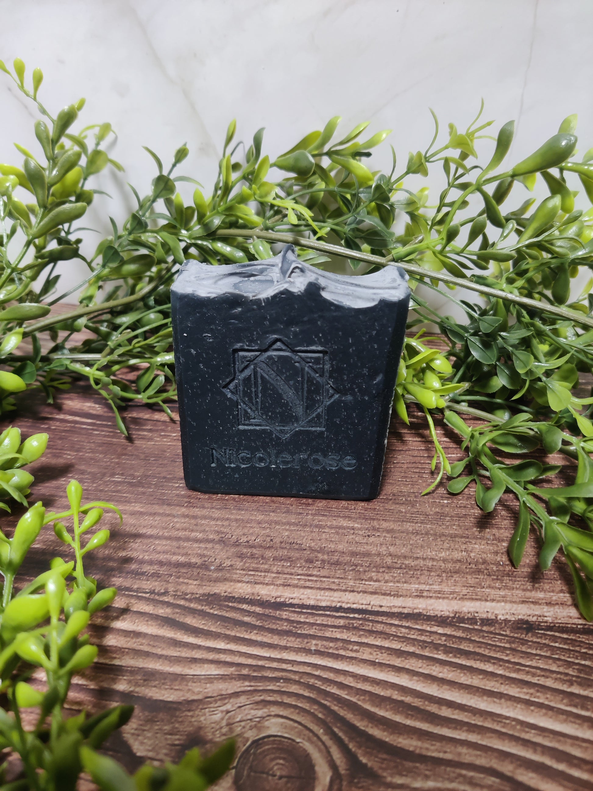 Black soap bar with a geometric logo on a wooden surface surrounded by green leaves