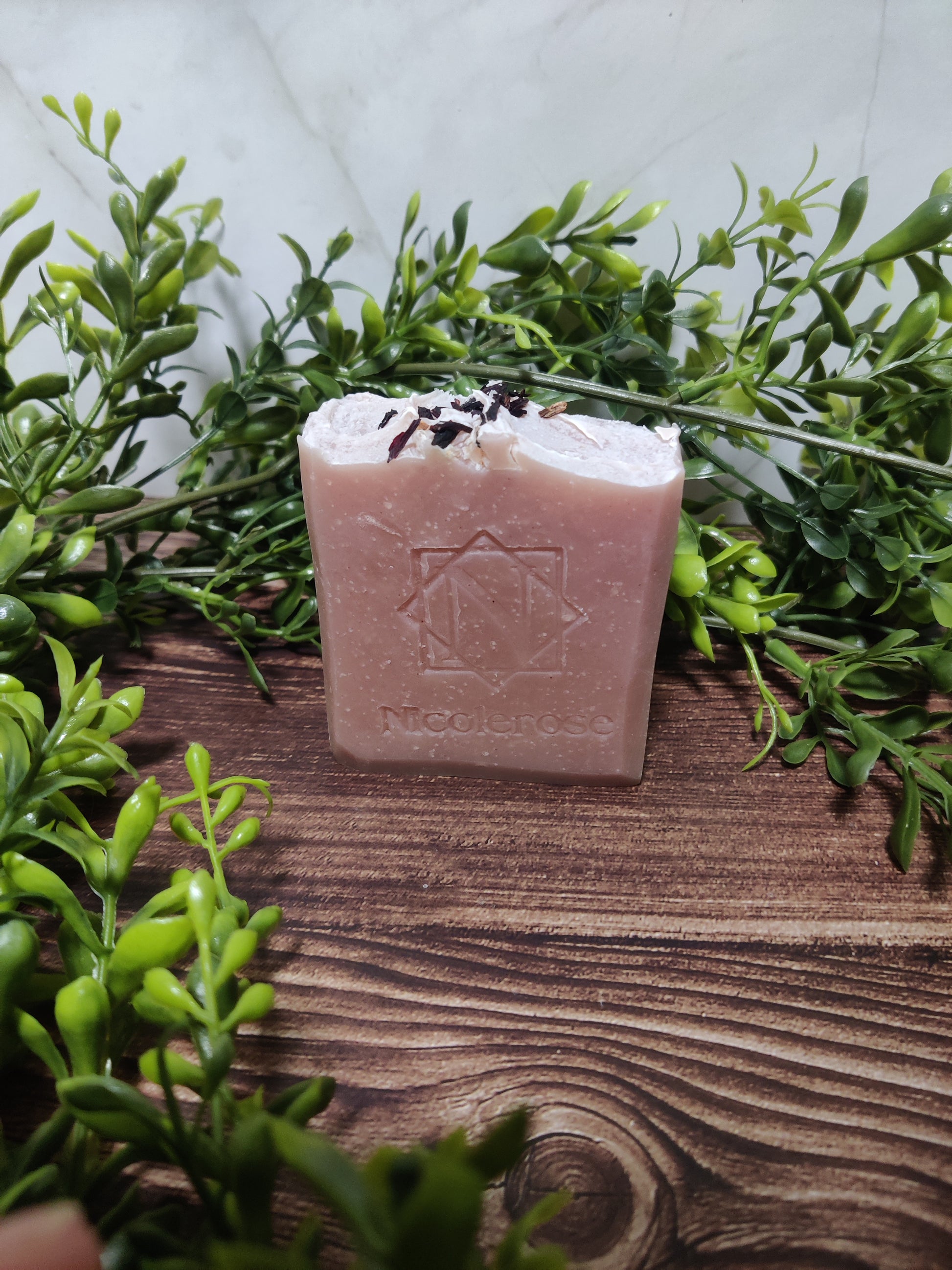 Bar of soap with a brand logo on a wooden surface surrounded by green leaves